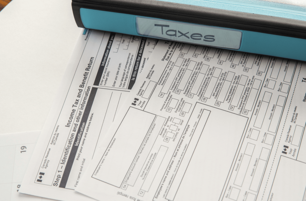 Pile of CRA tax forms with binder resting nearby on desk