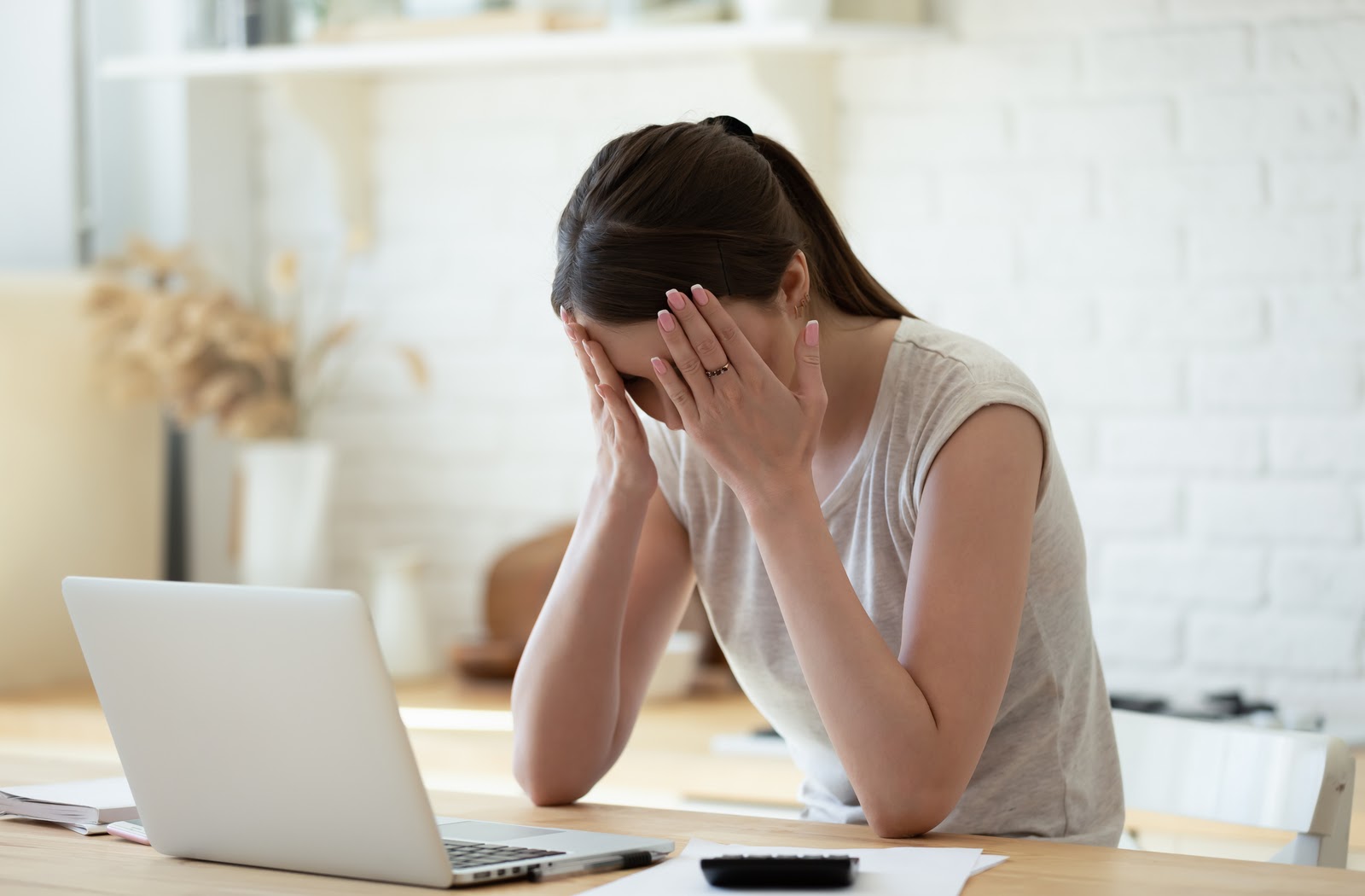 Upset woman sitting at laptop with head in hands after seeing credit score