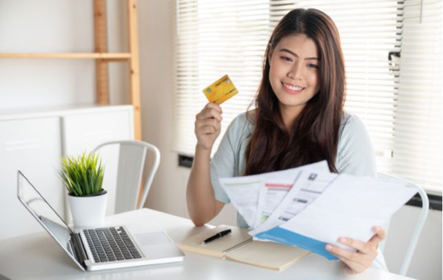 Young happy women holding papers with one hand and her credit card wit the other