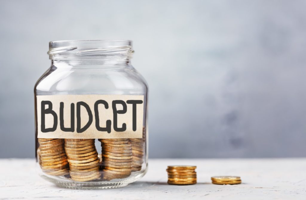 Money jar with "Budget" written on it and coins on the side and inside jar