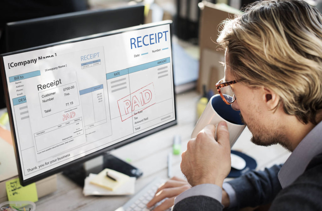 A male financial advisor at the bank is checking on his computer the current debts and liabilities of a client that is applying for a line of credit.