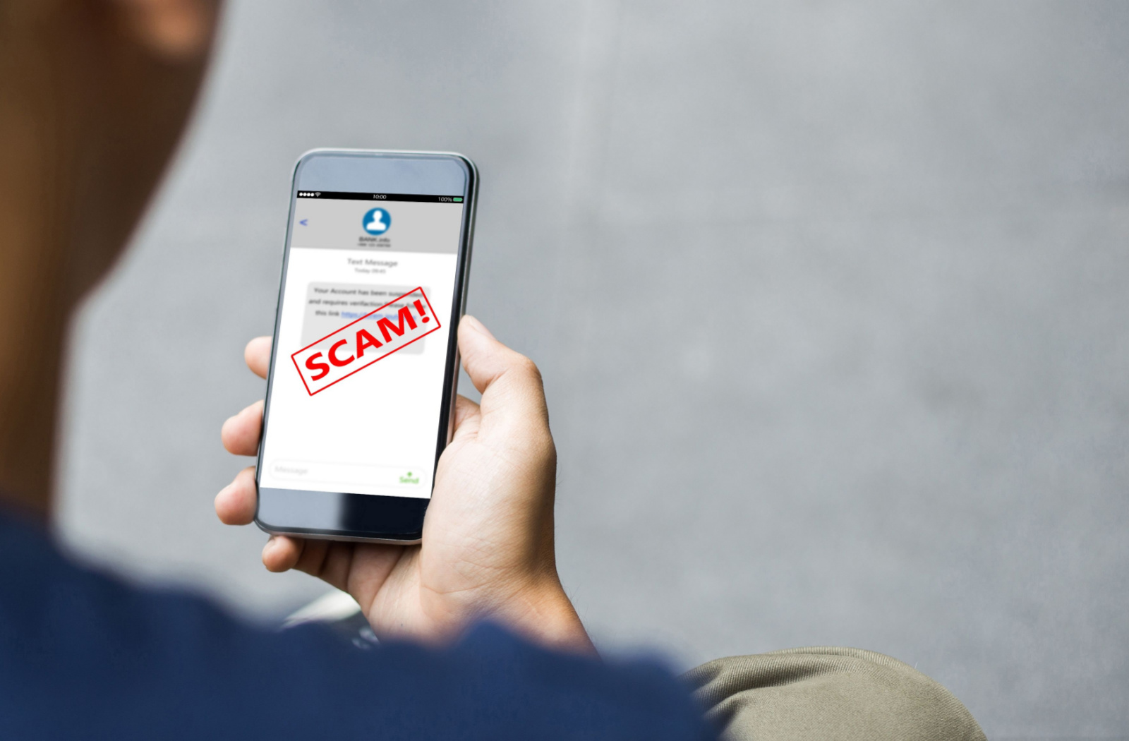 A close-up of someone holding a smartphone with a SCAM! warning message in red text across the screen