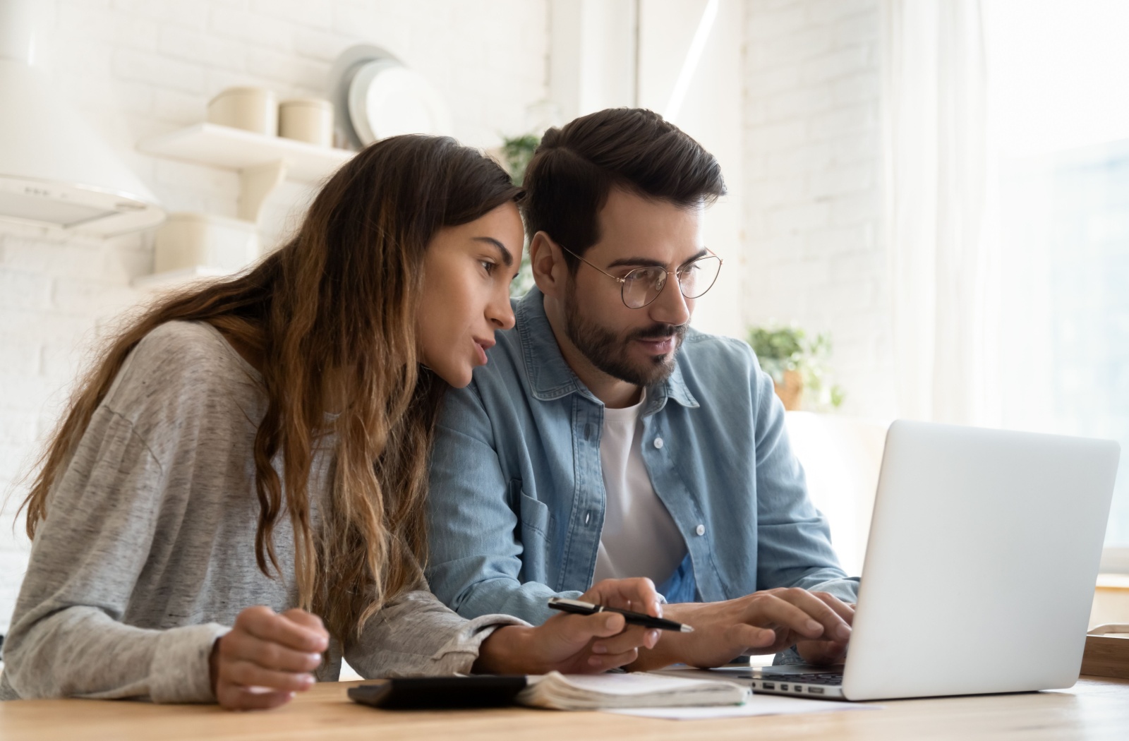 A couple in a brightly lit room looking over their savings and investments on a laptop to determine how they have been impacted by inflation.