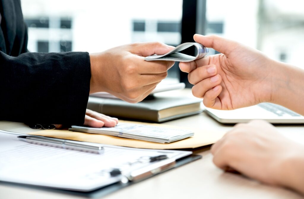 Close-up of a lender handing a person a cash loan over a desk that has a clipboard, pen, and papers on it.