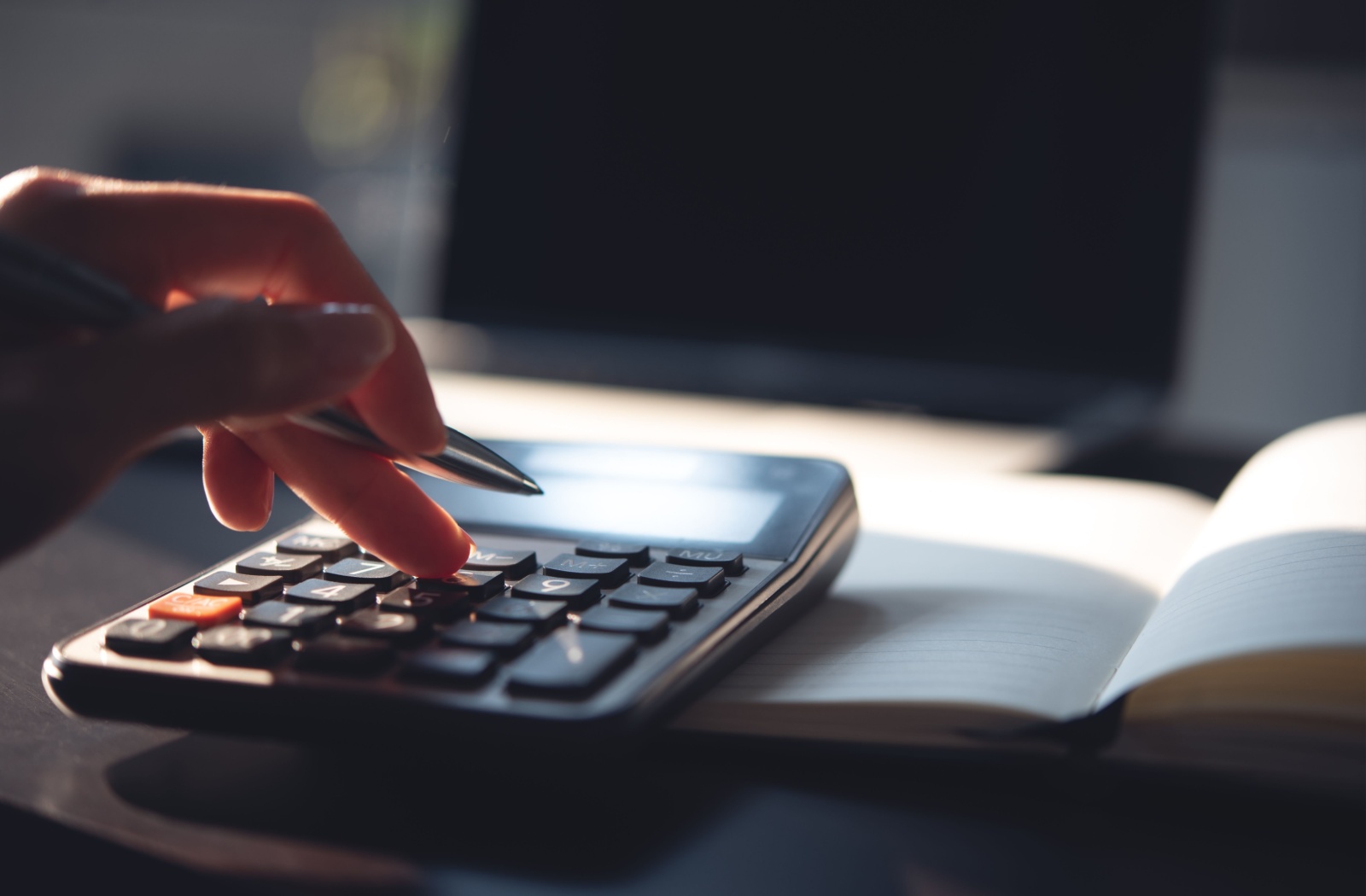 Close-up of a calculator on a desk while a person holds a pen and calculates the interest rate on their line of credit.