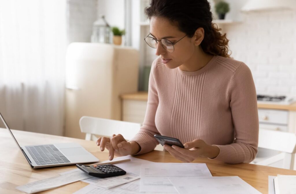 A person sitting down with a laptop, calculator, and lease agreement to organize monthly car payments