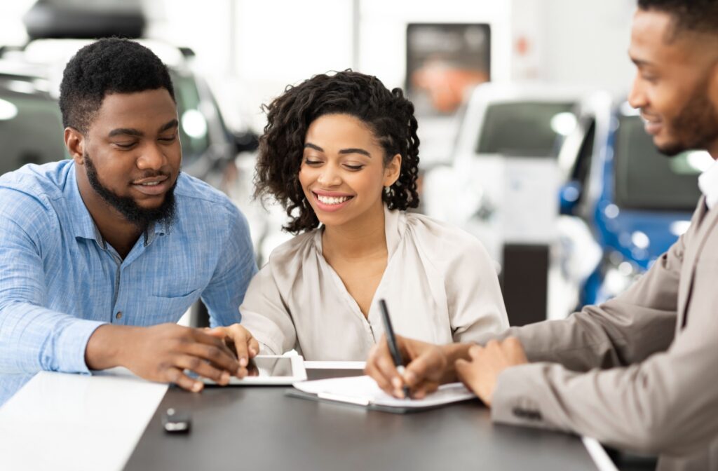 A couple sitting in a car dealership and signing papers to purchase a car
