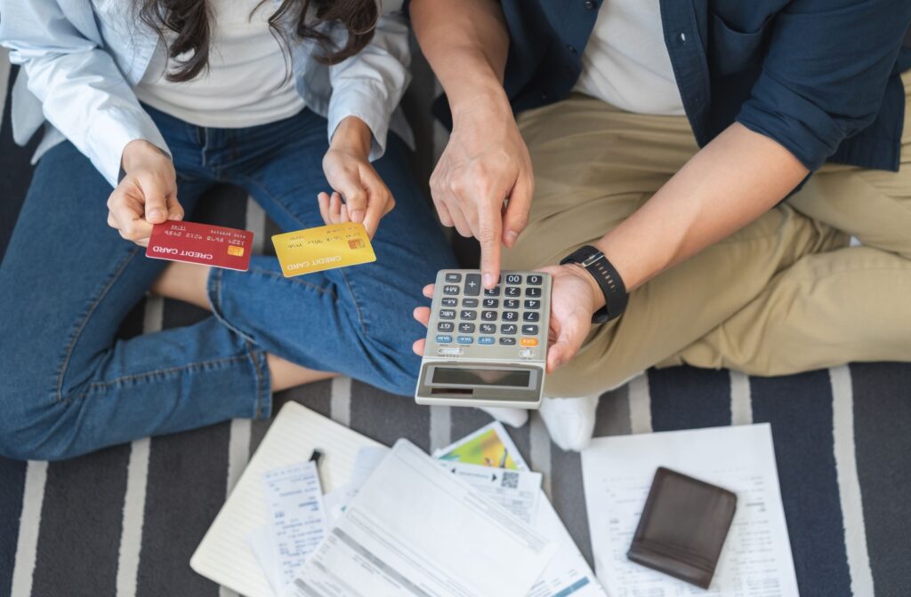Two people review bills and credit cards on the floor while using a calculator to work on paying off debt.