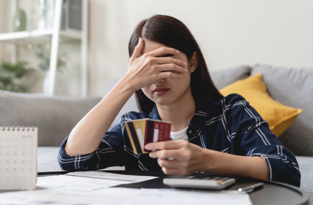 A person holds several credit cards and covers their face, appearing stressed about credit card debt, with bills and a calculator on the table.